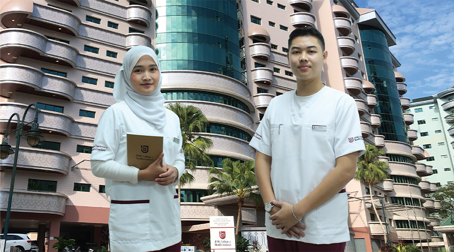 Nursing School in Asia | Smiling Asian male and female nursing students with notebook standing in front of school building and school signage JPMC College of Health Sciences