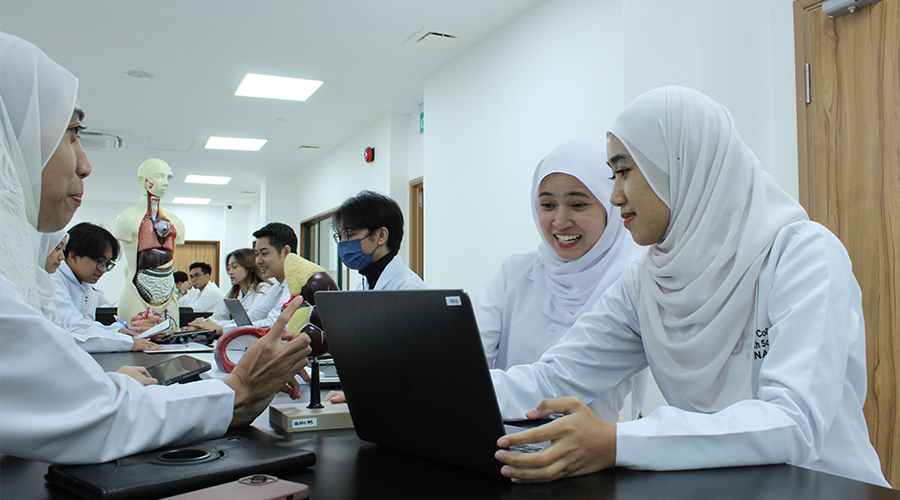 Nursing School Brunei | Male students female students in classroom laptop bench study nursing programme course model smiling lab coats