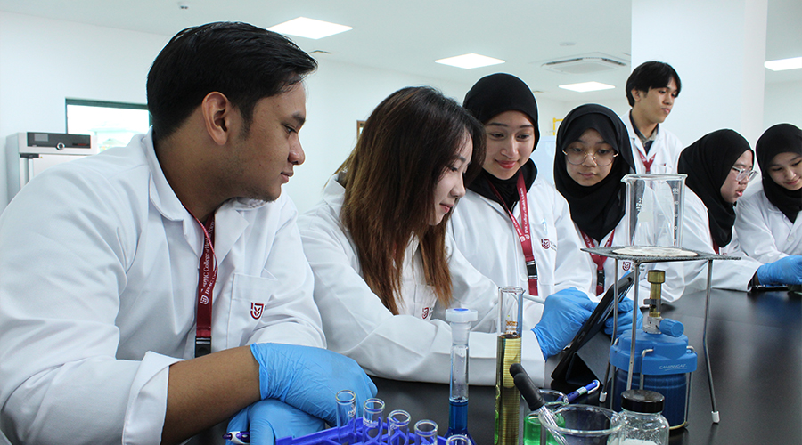 Nursing Course Brunei | smiling male students female students focus study JCHS lanyard bunsen burner beaker lab bench test tubes wire gauze blue surgical gloves