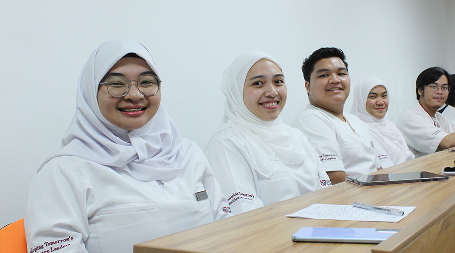 Nursing School Brunei | Male female JCHS students smiling school uniform glasses phones tablets pen and paper on table chair studying nursing classroom