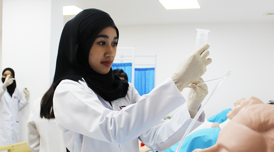 Nursing Course in Brunei | Female student JCHS black hijab clinical training nursing manikin hospital ward clinic classroom practice white latex gloves