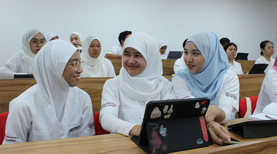 Nursing Course in Brunei | Male and female nursing students in a classroom sitting on benches with tablets and phones discussing the curriculum of the nursing programme at JCHS